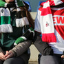 Ein Gladbach-Fan und ein Köln-Fan sitzen in Fankleidung nebeneinander