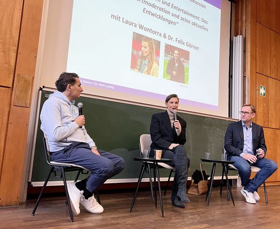 Laura Wontorra sitzt im Hörsaal und hält ein Mikro in der Hand
