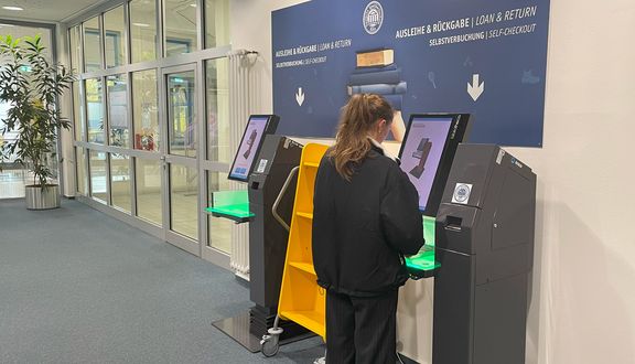 Frau steht an einem Selbstverbucherterminal in der Bibliothek
