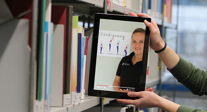 Zwei Hände nehmen ein Tablet aus einem Bücherregal