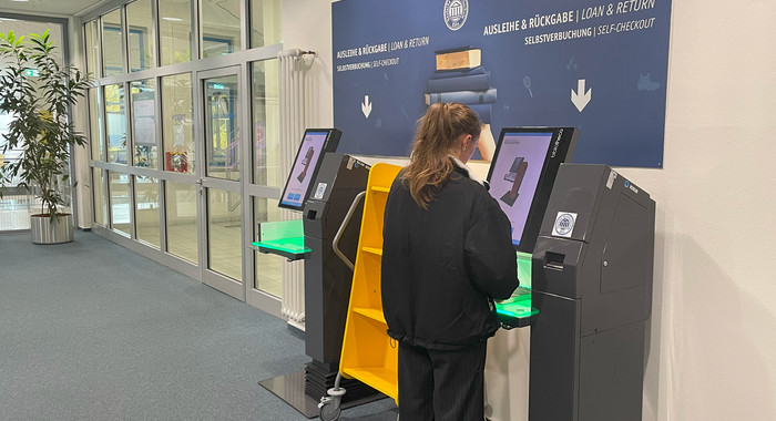 Frau steht an einem Selbstverbucherterminal in der Bibliothek