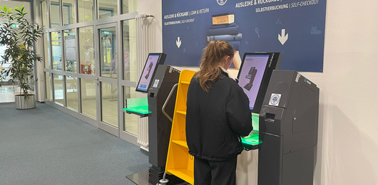 Frau steht an einem Selbstverbucherterminal in der Bibliothek