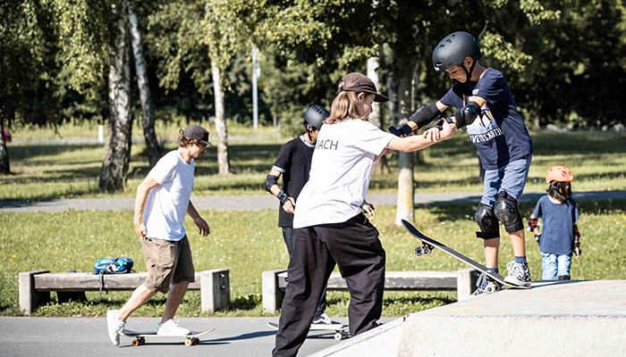 Lehrerin gibt Schüler Hilfestellung beim Skateboarding auf einer Rampe.