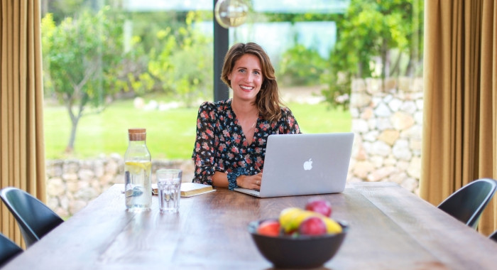 Lena Kadlec sitzt mit Laptop an einem Holztisch und schaut in die Kamera