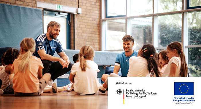 Kinder in einer Sporthalle sitzen auf dem Boden in einem Kreis