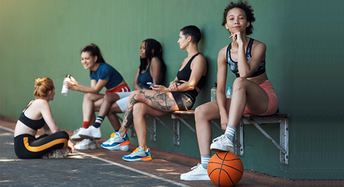 Symbolbild - sportlich gekleidete Jugendliche sitzen auf einer Bank, Basketball im Vordergrund