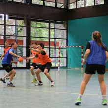 Beim Handballspiel greifen zwei Handballspieler mit blauen Leibchen auf 3 Handballspieler mit orangenen Leibchen an
