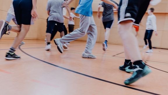 Kinder laufen in einer Sporthalle.

