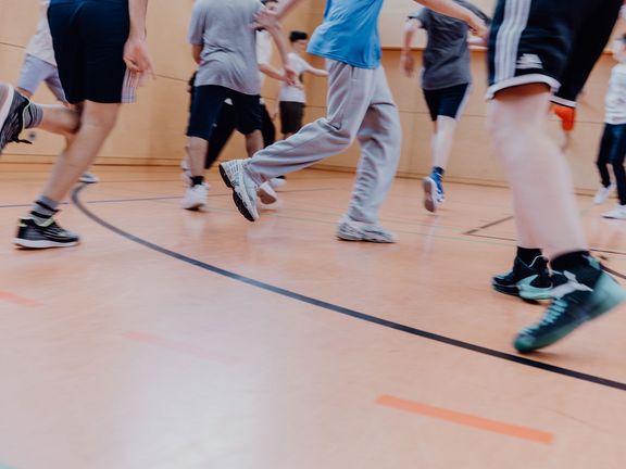 Kinder laufen in einer Sporthalle.
