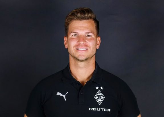 Das Bild zeigt ein Porträt von Daniel Mair. Ein blonder Mann in einem schwarzen Polo-Shirt von Borussia Mönchengladbach vor einem dunkelgrauen Hintergrund.
