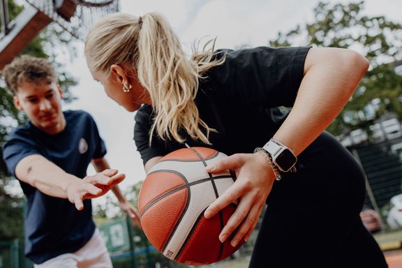 Foto von Basketballspielszene bei der eine Frau den Basketball vor einem verteidigenden Mann wegstreckt
