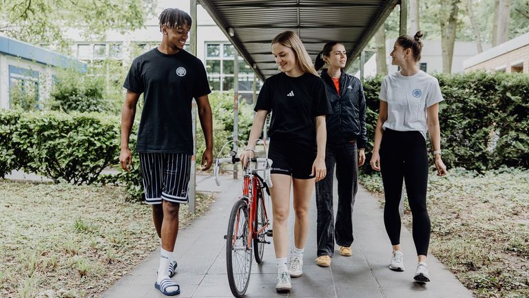 Vier Studierende gehen mit einem Rennrad über den Campus der Deutschen Sporthochschule
