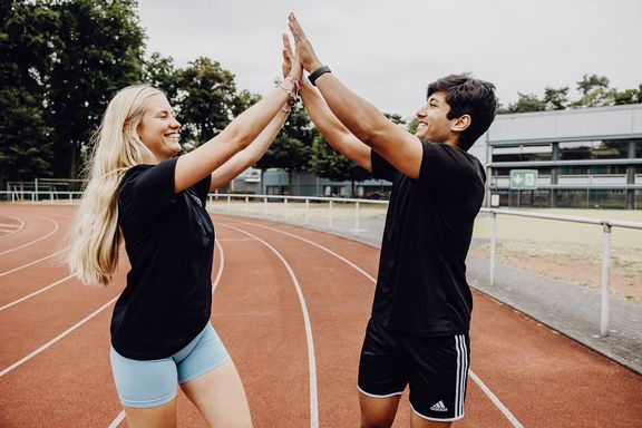 Zwei Studierende im Sportoutfit klatschen sich ab 
