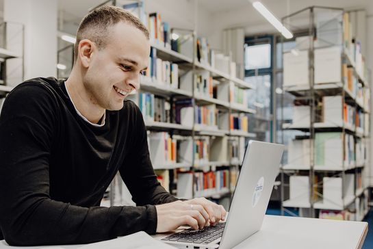 Student lernt mit Laptop in der Bibliothek der Deutschen Sporthochschule