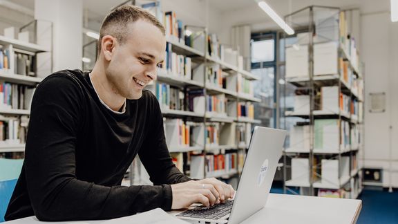 Student lernt mit Laptop in der Bibliothek der Deutschen Sporthochschule
