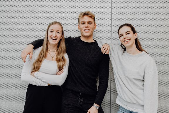 Drei Studierende stehen Arm in Arm nebeneinander
