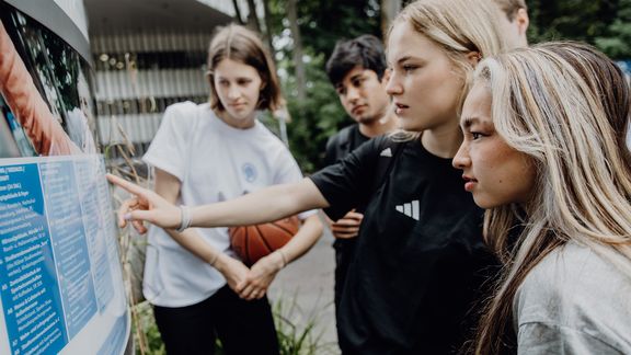 Einige Studierende betrachten den Wegweiser im Eingangsbereich der Deutschen Sporthochschule
