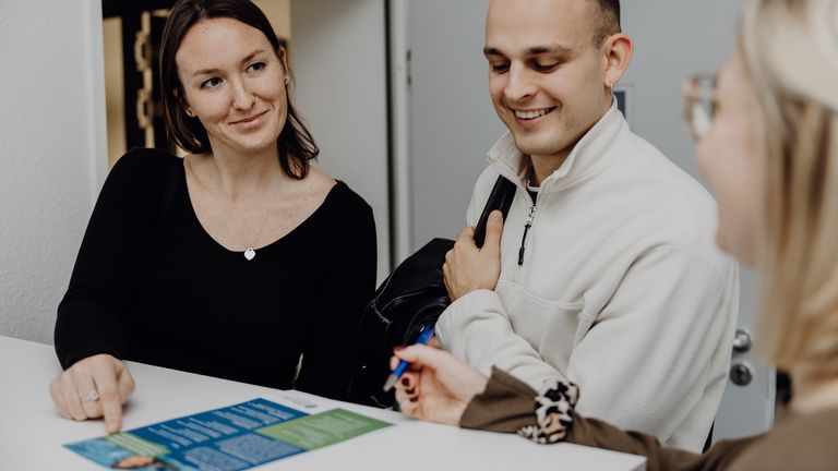 Foto von drei Personen die einen Flyer auf dem Tisch betrachten
