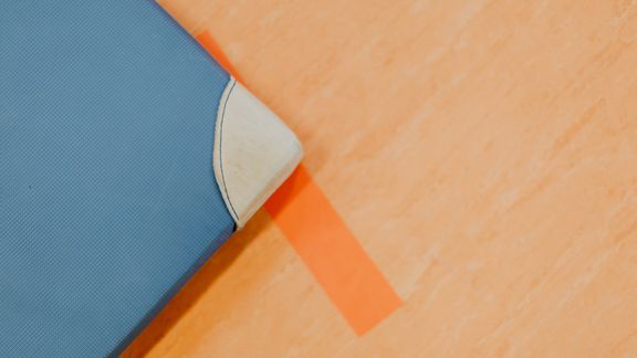Blaue Turnmatte liegt über orangenem Strich auf Hallenboden
