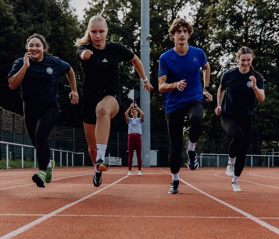 Foto von Personen die auf der Laufbahn nebeneinander zum Sprint ansetzen

