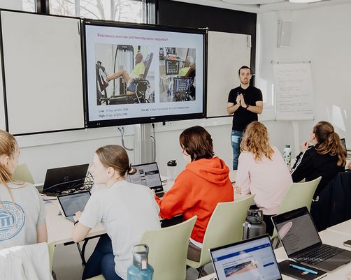 Studierende sitzen im Seminar und hören Dozierendem zu
