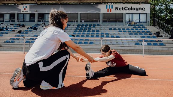 Trainerin hilft Frau bei Dehnübung im Stadion
