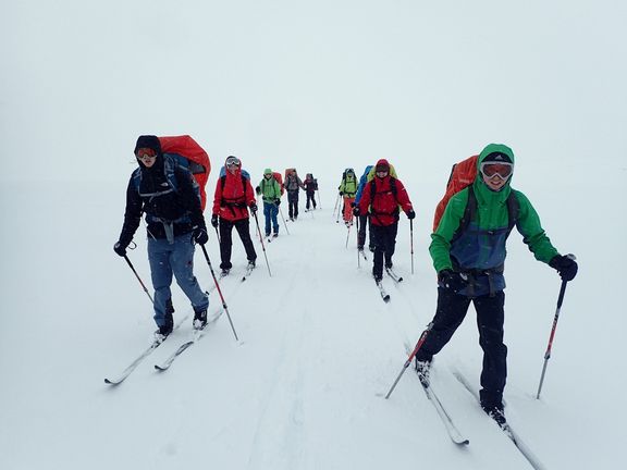 Gruppe von Skifahrern mit Rucksäcken in Schneelandschaft bei schlechter Sicht
