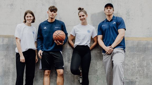 Studierende der Deutschen Sporthochschule Köln stehen gemeinsam an einer Wand, eine Person mit Basketball.
