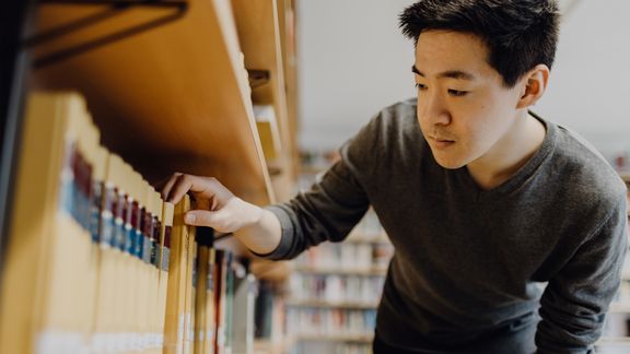 Eine Person zieht ein Buch aus dem Bücherregal 
