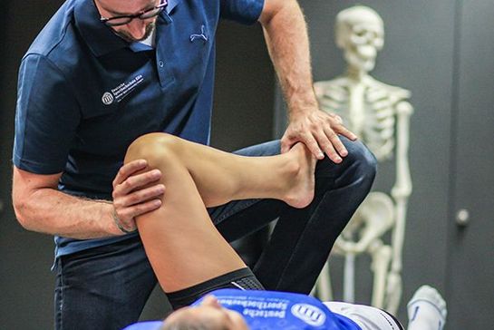 Mann untersucht das Knie einer Frau
