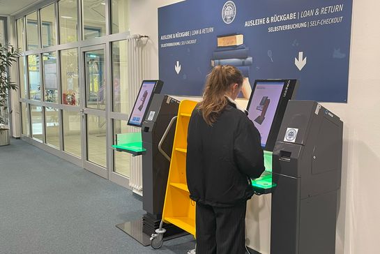 Frau steht an einem Selbstverbucherterminal in der Bibliothek