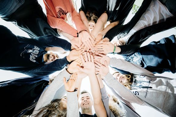 Im Kreis stehende Studierende legen die Hände in der Mitte übereinander
