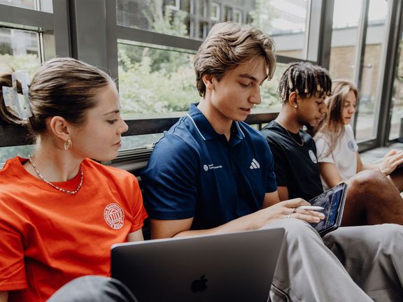 Drei Studierende arbeiten mit Laptops im Foyer der Deutschen Sporthochschule
