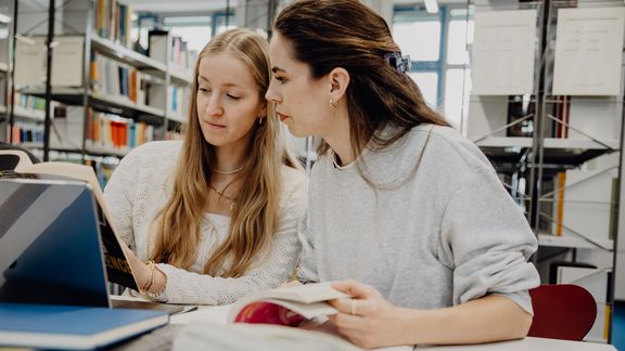 Zwei Studentinnen lesen ein Buch in der Bibliothek der Deutschen Sporthochschule

