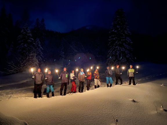 Gruppe von Menschen steht nachts im Schnee und hält Fackeln in der Hand
