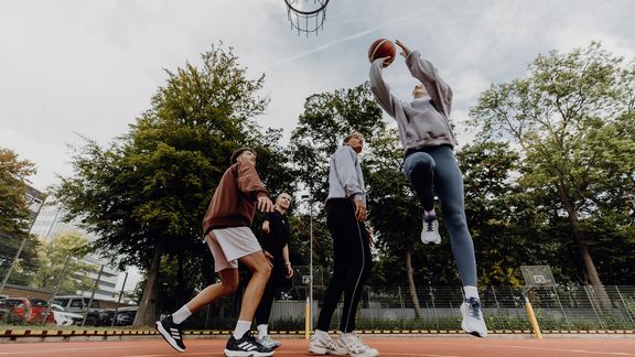 Foto einer Basketballspielszene bei der eine Frau vor den Verteidigenden hochspringt und zum Wurf ansetzt
