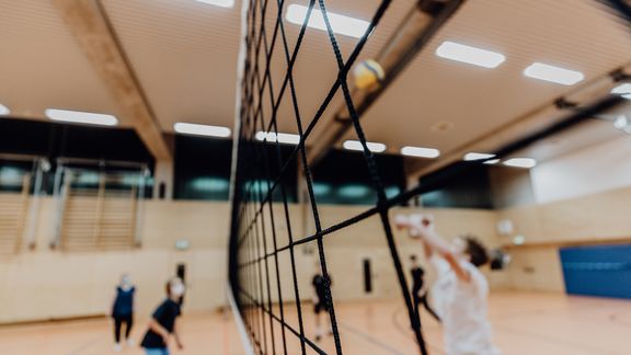 Kinder spielen Volleyball über ein Netz in einer Halle
