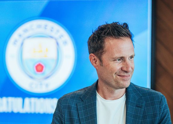 Bild von Thomas Krücken. Ein Mann in einem Blauen Jacket. Im Hintergrund ist ein Bildschirm mit einem Manchester City Logo zu sehen. 
