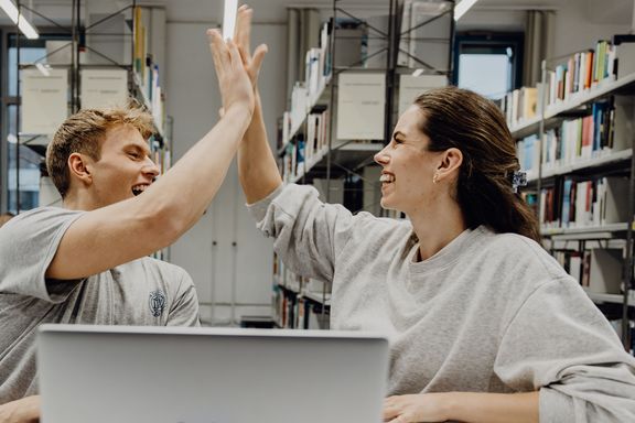 Zwei Studierende geben sich ein High-Five in der Bibliothek
