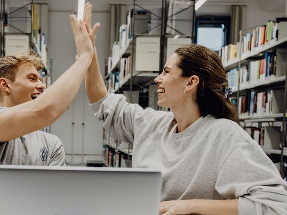 Zwei Studierende geben sich ein High-Five in der Bibliothek
