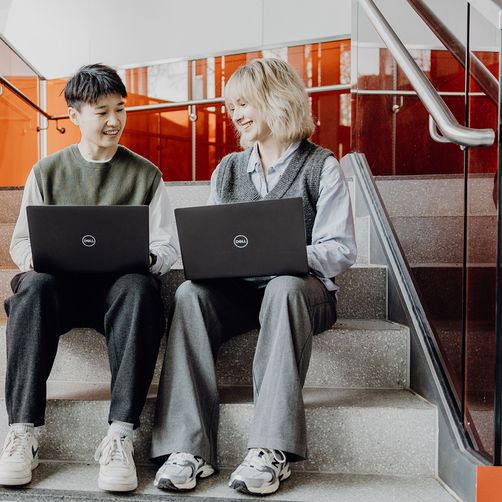 Studierende sitzen mit Laptops auf dem Schoß im Treppenhaus
