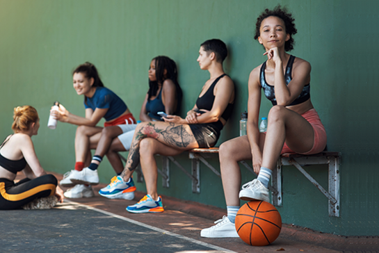 Symbolbild - sportlich gekleidete Jugendliche sitzen auf einer Bank, Basketball im Vordergrund
