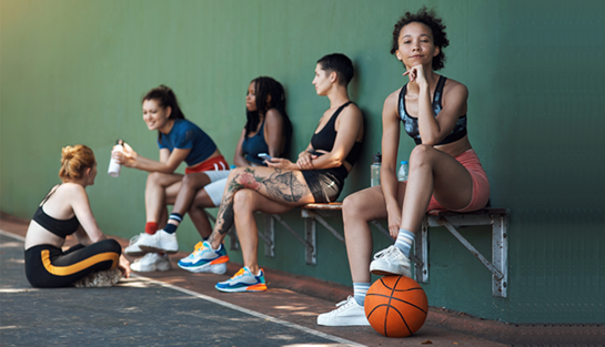Symbolbild - sportlich gekleidete Jugendliche sitzen auf einer Bank, Basketball im Vordergrund
