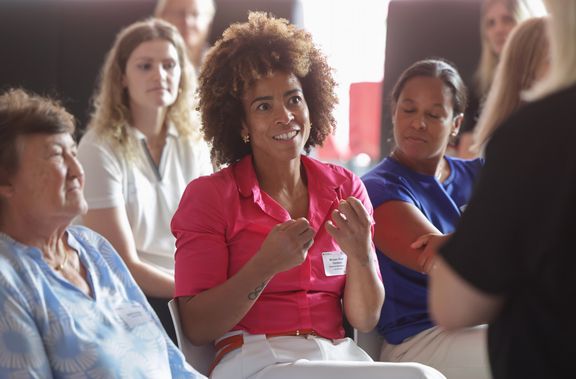 ein diverses Publikum (alte und junge Personen, weiße und Women-of-Colour), eine Woman-of-Colour macht einen Beitrag zur Diskussion
