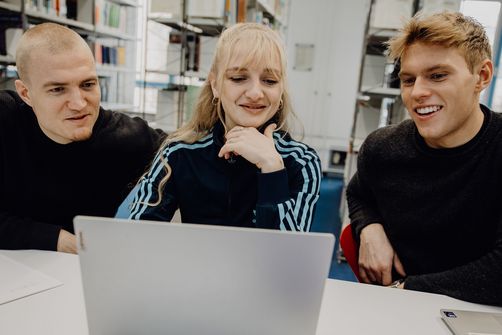 Drei Studierende sitzen vor einem Laptop in der Bibliothek der Deutschen Sporthochschule
