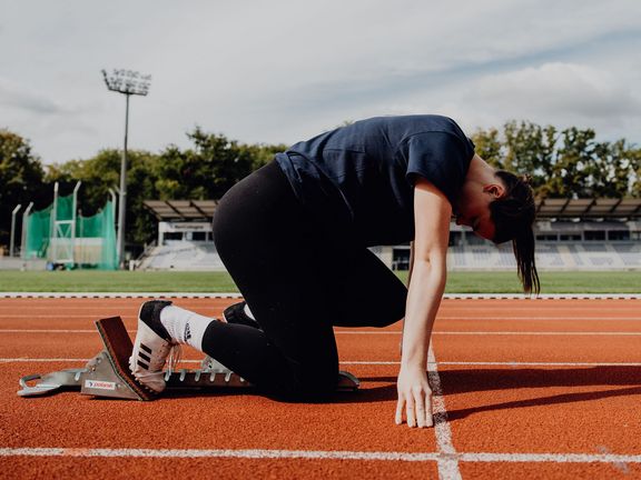 Seitliches Foto von Person die im Startblock bereit zum Start ist

