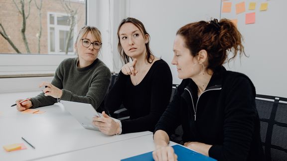 Foto von drei Personen die im Besprechungsraum sitzen 

