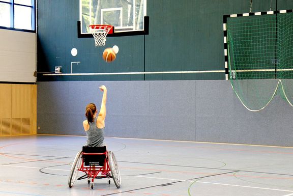 In einer Halle sieht man eine Rollstuhlfahrerin von hinten mit nach oben au
