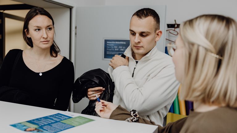 Foto von drei Personen die um einen Tisch mit einem kleinen Flyer sitzen
