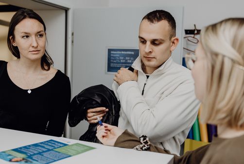 Foto von drei Personen die um einen Tisch mit einem kleinen Flyer sitzen
